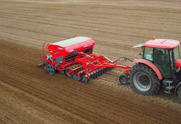 Siewnik mechaniczny ciężki Unia AMBER DUPLO na polu z ciągnikiem w pracy Siewnik mechaniczny ciężki Unia AMBER DUPLO na polu w pracy